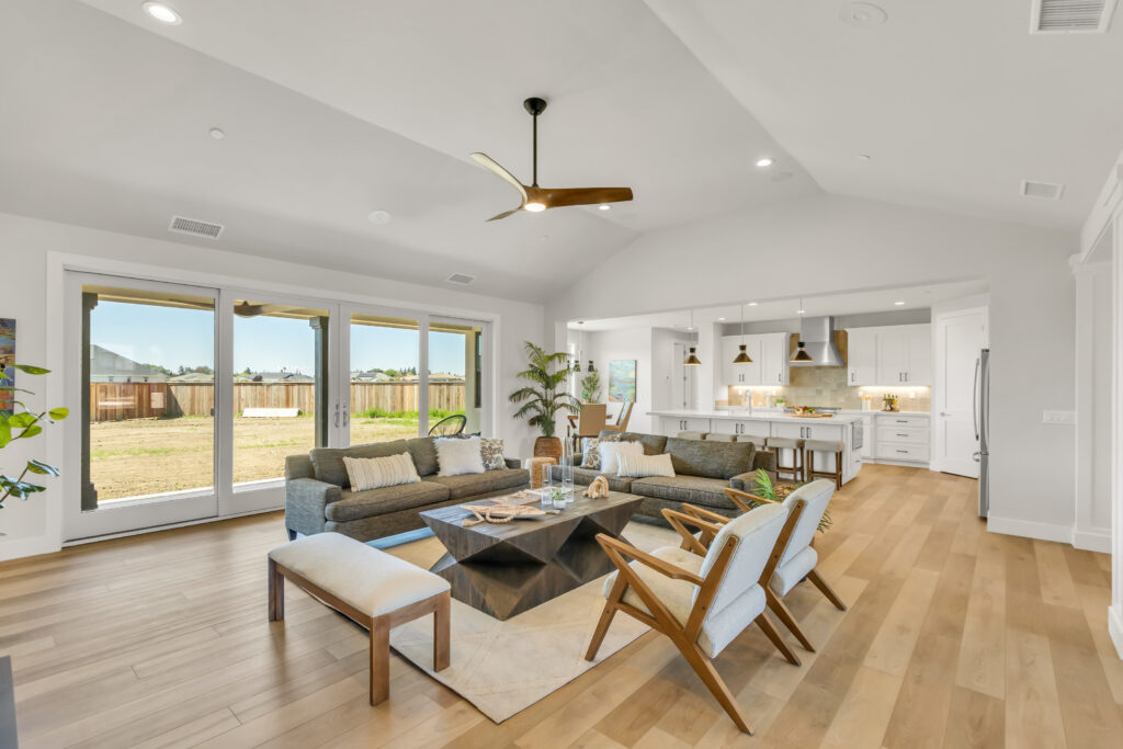 Living room with a mid-century modern vibe. It features two large sofas, two chairs, a bench, and a large geometic coffee table. In the background the kitchen is visible.