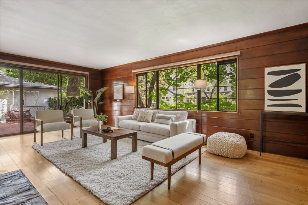 Mid-century inspired staging for a beautiful home's living room featuring a sofa, two floor lamps, chairs, and a bench along with floor plants, artwork, and accessories.