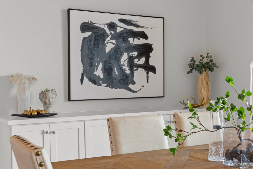 Black and white artwrok over a console in the background with accessories and a glimpse of a dining table and chairs in the foreground.