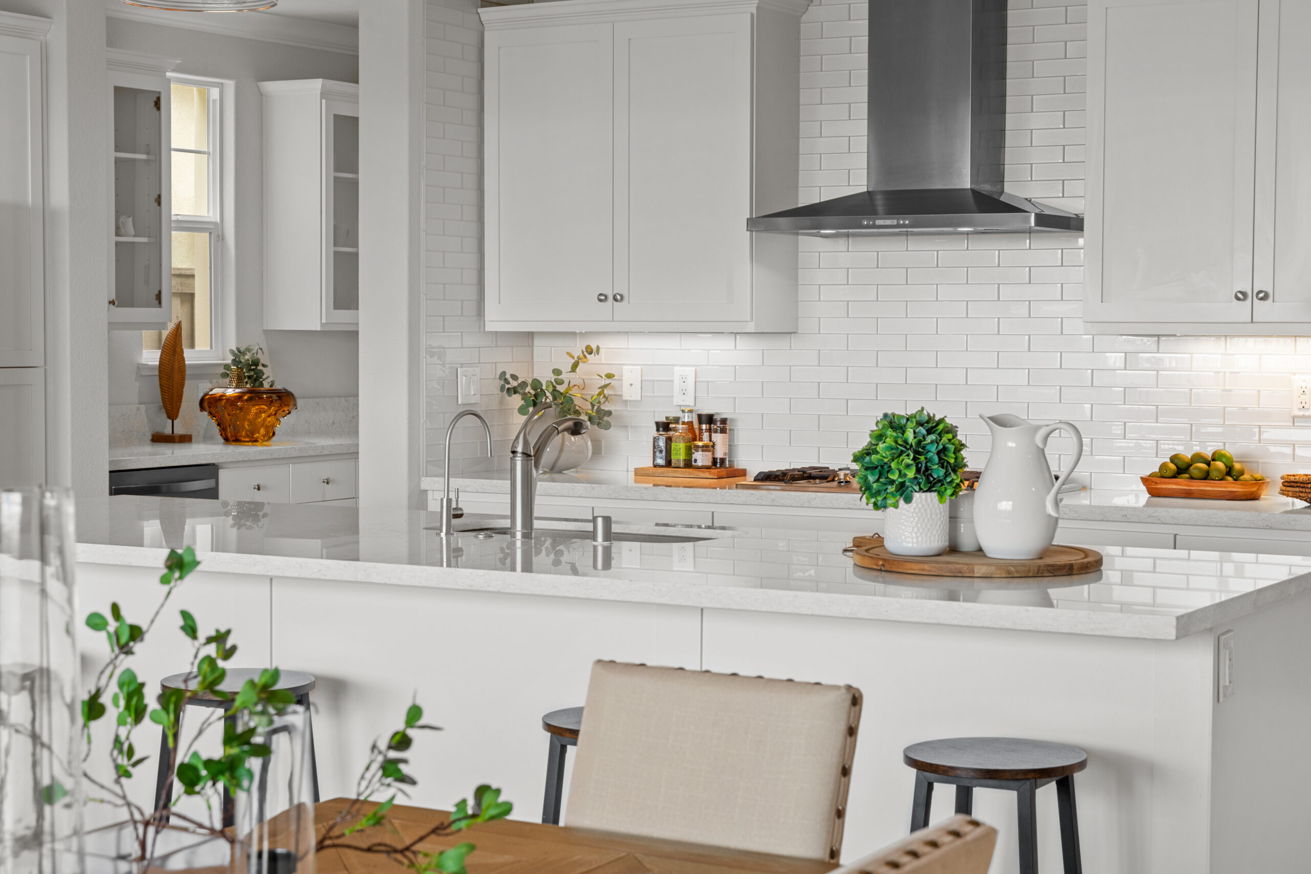 Kitchen with white subway tiles, cabinets, and counters. Barstools are it fron tof the island and a dining table and chairs are slightly visible in foreground.