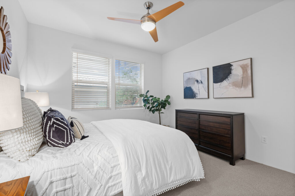Lush bed in neutral tones with mirror above and a dresser with artwork above.