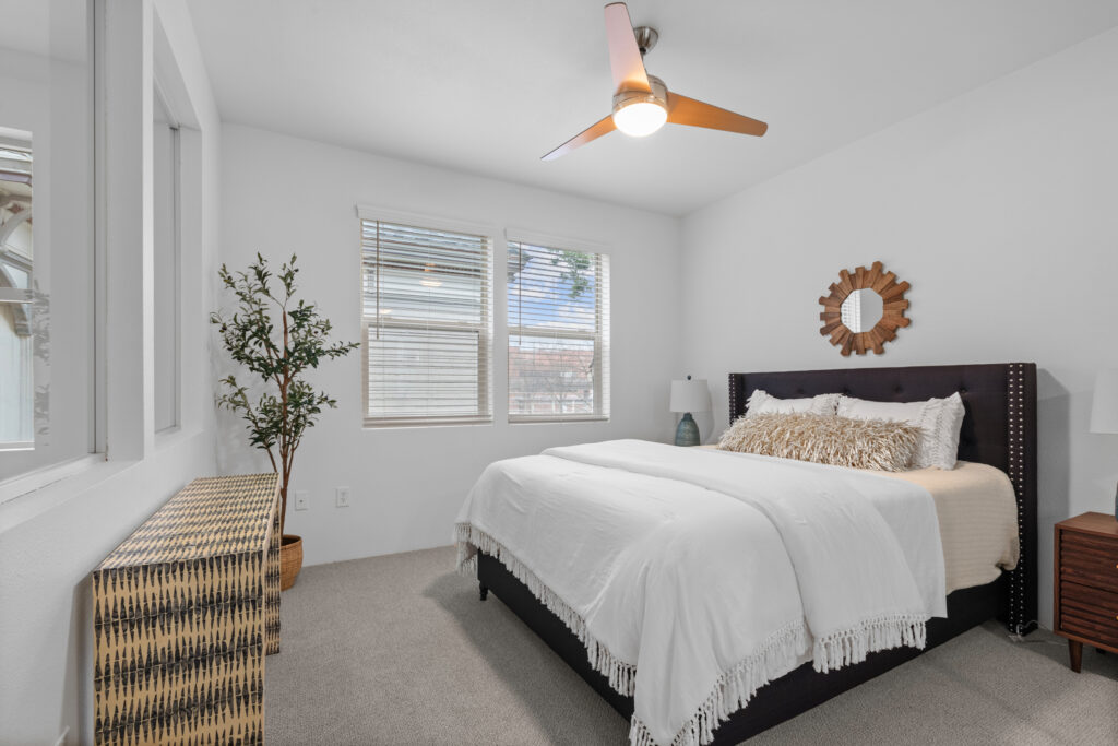 Bedroom with a bed on the right featuring a fringy comforter and a mirror over the bed and a console on the left.