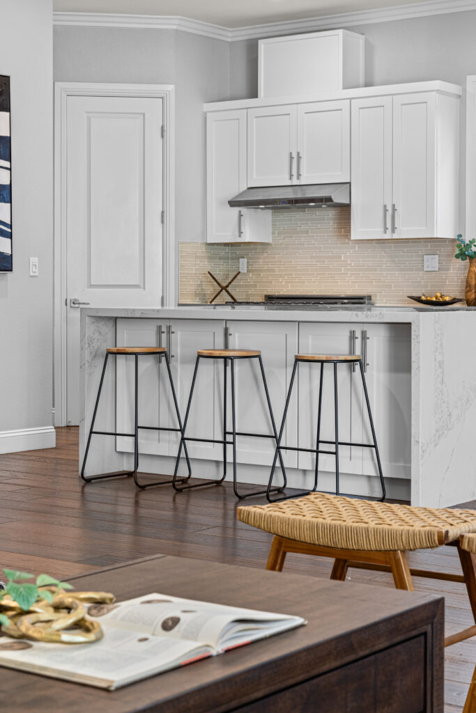 in the foreground there is a coffee table; beyond there is a kitchen featuring an island with three barstools.