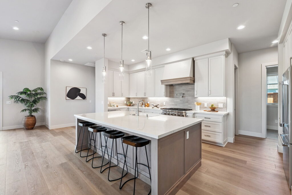 Kitchen with four barstools at the island in foreground and three pendants hanging over it.
