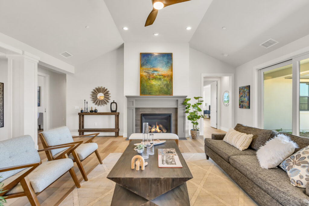 Living room with angular coffee table flanked by chairs to left and sofa to the right. In the background there is a fireplace with artwork above and a console to the left of that