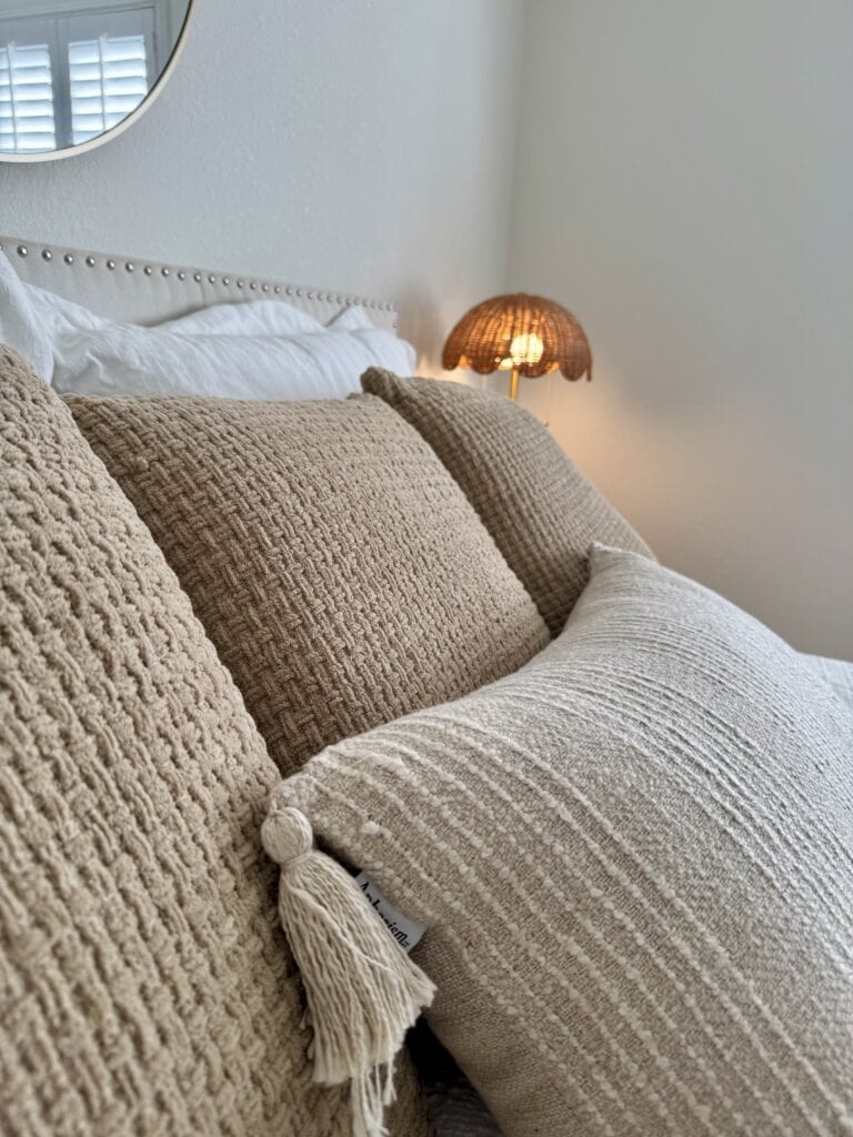 Neutral textured decorative pillows in a staged bedroom create a cozy, inviting atmosphere.