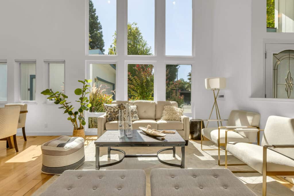 Living room with sofa under very tall stacked windows. There is also a coffee table, chairs, lighting, a floor plant, and benches in the foreground.