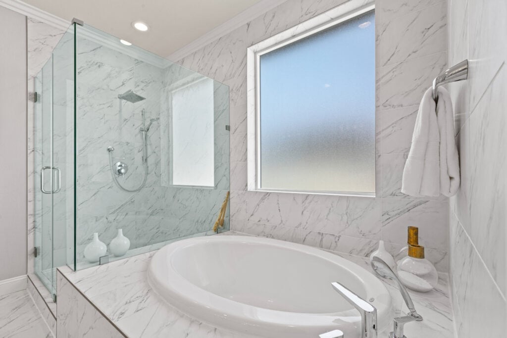 Bright, luxurious bathroom featuring marble tiles, a bathtub, and a frosted window for home staging.